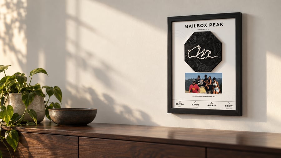 Framed Mailbox Peak piece with a black 3D-printed terrain octagon and a raised ivory trail line, hanging above a walnut sideboard in warm afternoon light.